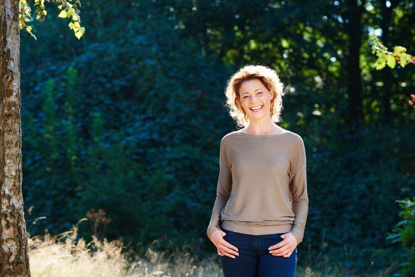 Middle aged woman in brown sweater posing in woods