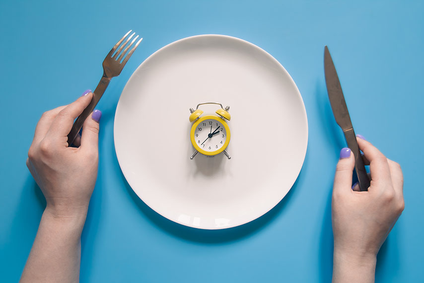 hands holding a knife and a fork to eat a clock
