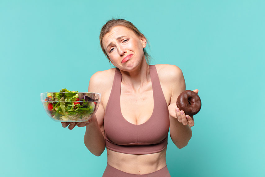sporty young woman holding salad and a donut