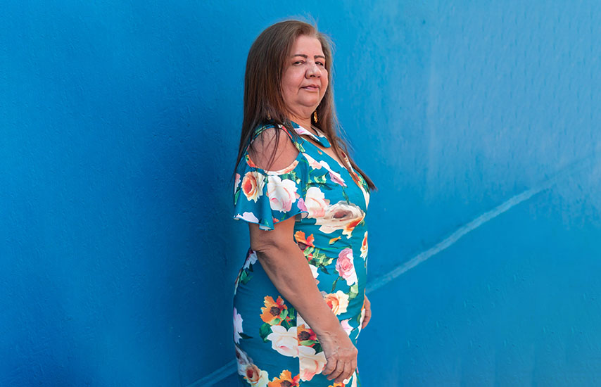 Older aged woman in dress posing by the blue wall